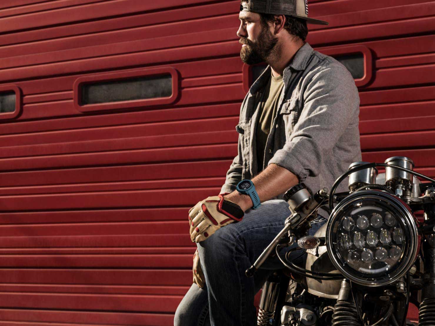 Man leaning on motorcycle wearing Garmin smartwatch.